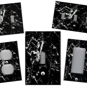 May include: A collection of black marble-patterned light switch covers and outlet covers. The covers feature a glossy finish with white veining. Various configurations include toggle switches, rocker switches, and electrical outlets. Each cover has a silver screw.