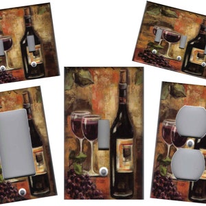 May include: A set of light switch and outlet covers featuring a painting of a wine bottle, two glasses of red wine, and grapes. The background is a warm, earthy tone with hints of brown, orange, and yellow.