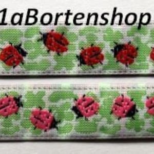 Può includere: Due strisce di tessuto verde e bianco con un motivo ripetuto di coccinelle rosse. Il tessuto è tessuto con un piccolo motivo a nido d'ape bianco. Il testo "1aBortenshop©" è stampato sulla striscia superiore.