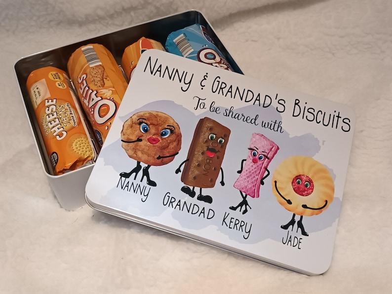 May include: A white metal tin with a colorful illustration of biscuits with faces. The text on the tin reads "Nanny & Grandad's Biscuits" and "To be shared with".  The names "Nanny", "Grandad", "Kerry", and "Jade" are written below the biscuits.