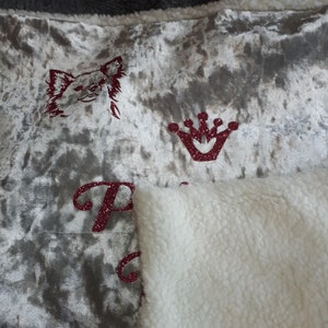 May include: A plush throw blanket with a silver velvet side and a white sherpa side. The velvet side features a red glitter crown, a red glitter chihuahua, and the word "Princess" in red glitter.