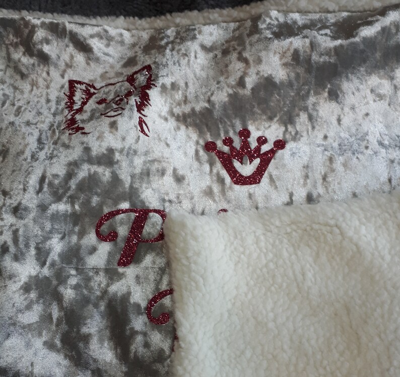 May include: A plush throw blanket with a silver velvet side and a white sherpa side. The velvet side features a red glitter crown, a red glitter chihuahua, and the word "Princess" in red glitter.