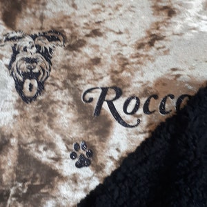 May include: A brown and white patterned dog bed with a black and white dog silhouette, a paw print, and the name "Rocco" embroidered in black.