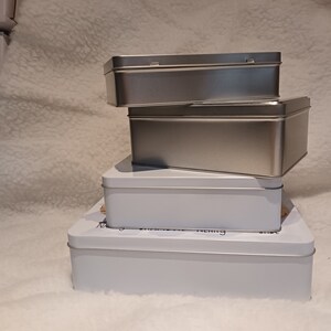 May include: Three silver and white rectangular boxes stacked on top of each other. The top two boxes are silver and the bottom box is white.