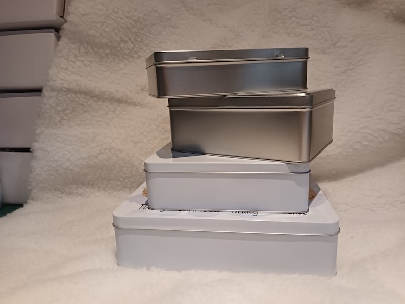 May include: Three silver and white rectangular boxes stacked on top of each other. The top two boxes are silver and the bottom box is white.
