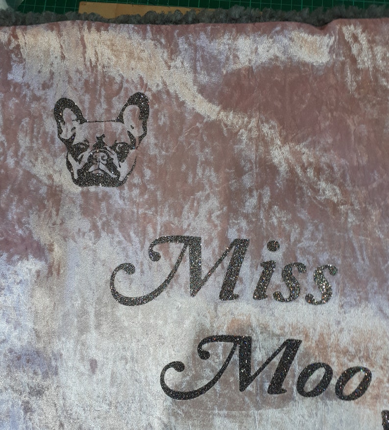 May include: A light pink velvet throw blanket with a black and white image of a French Bulldog and the text "Miss Moo" in black glitter.