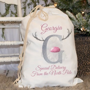 May include: White canvas Santa sack with a pink and silver reindeer design. The sack has the name "Georgia" and the text "Special Delivery From the North Pole" printed on it.