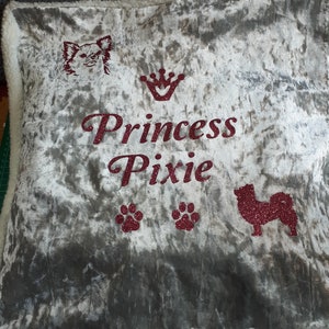 May include: A gray velvet pillow with a white border. The pillow has a pink glitter design of a dog, a crown, paw prints, and the text "Princess Pixie".