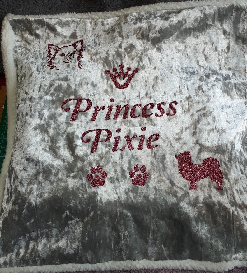 May include: A gray velvet pillow with a white border. The pillow has a pink glitter design of a dog, a crown, paw prints, and the text "Princess Pixie".