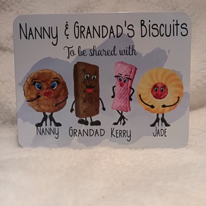 May include: A white sign with the text "Nanny & Grandad's Biscuits To be shared with" and four cartoon biscuits with faces. The biscuits are labeled "Nanny", "Grandad", "Kerry", and "Jade".