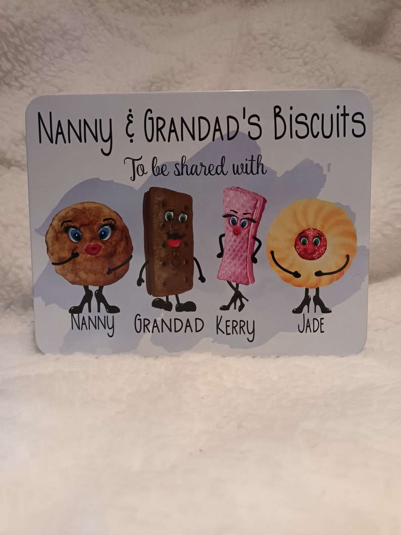 May include: A white sign with the text "Nanny & Grandad's Biscuits To be shared with" and four cartoon biscuits with faces. The biscuits are labeled "Nanny", "Grandad", "Kerry", and "Jade".