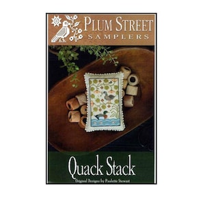 Może przedstawiać: Wzór haftu krzyżykowego zatytułowany "Quack Stack" autorstwa Plum Street Samplers. Projekt przedstawia dwie kaczki w stawie, otoczone elementami kwiatowymi. Wzór jest wyświetlany na małej, prostokątnej poduszce z tekstem "Quack Stack" poniżej.