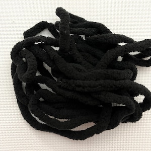 May include: A close-up of a pile of black fuzzy yarn. The yarn is soft and fluffy, and it is perfect for crocheting or knitting.