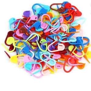 May include: A collection of brightly coloured plastic stitch markers. The markers are in shades of red, blue, yellow, green, and purple. These small, curved markers are used in knitting and crochet to mark stitches or rows. The markers are in a variety of shapes.
