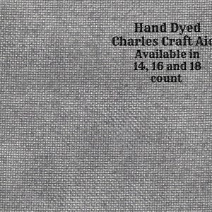 Puede incluir: Primer plano de una tela gris con textura tejida. El texto "Hand Dyed Charles Craft Aida Available in 14, 16 and 18 count" está impreso en la tela.