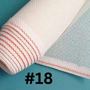May include: A roll of white needlepoint canvas fabric featuring a distinct grid pattern and a single horizontal orange thread woven near the edge. The number #18 is printed in black text at the bottom of the image, indicating the mesh count.