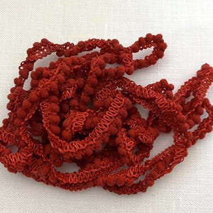 May include: Red pom-pom trim with a ruffled edge. The trim is made of soft, fuzzy material and is perfect for adding a touch of whimsy to any project.