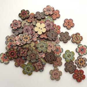May include: A selection of wooden flower-shaped buttons in a variety of colours and patterns. The buttons display detailed designs in shades of red, brown, green, and blue. One button is a natural wood colour.