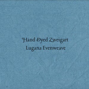 May include: A square of light blue fabric with the text "Hand Dyed Zweigart Lugana Evenweave" in black. The fabric has a fine, even weave, and the overall appearance is smooth and slightly textured.
