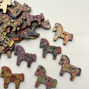 May include: Wooden horse-shaped buttons in various colors and patterns. The buttons feature designs such as swirls, stars, and floral motifs. Some horses have rainbow manes, while others have solid-colored manes. These decorative buttons are ideal for crafts and sewing projects.