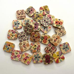 May include: A collection of square wooden buttons with floral and geometric patterns in various colors. Each button has two or four holes for sewing. The buttons feature designs of flowers, dots, and other decorative elements.