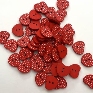 Puede incluir: Un conjunto de botones de madera rojos en forma de corazón con lunares blancos. Cada botón tiene dos agujeros para coser. La disposición dispersa resalta su diseño. Ideales para proyectos de manualidades, estos botones añaden un toque encantador.