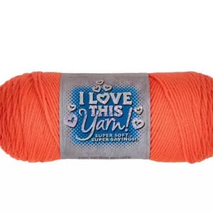 May include: A skein of bright orange yarn wrapped with a paper label that reads I LOVE THIS YARN! SUPER SOFT... SUPER SAVINGS! FREE PATTERN INCLUDED. The label features a blue background with white text and small heart icons surrounding the main title.