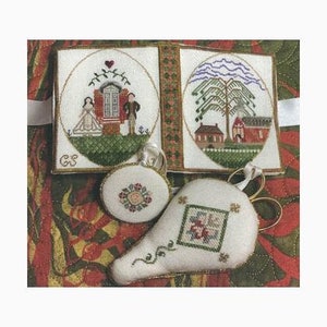 May include: A set of embroidered needlework items including a rectangular folding case with two oval scenes of a couple and a tree, a small circular pincushion with a floral motif, and a pear-shaped pincushion featuring a central square floral design.