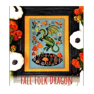 May include: Framed cross-stitch art featuring a green dragon with orange and yellow accents, surrounded by mushrooms and flowers on a light blue background. The artwork is framed in black with an orange border. The text "FALL FOLK DRAGON" is at the bottom.