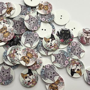 以下が含まれることがあります： 猫のイラストが描かれた木製ボタンのコレクション。ボタンには、さまざまな猫の種類と、グレー、ブラウン、ブラック、ホワイトの色合いの花柄のデザインが施されています。縫い付け用の穴が2つあるボタンもあります。ボタンは丸く、明るい色の木材で作られています。
