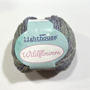 May include: A ball of Lighthouse Wildflowers yarn in shades of gray, green, and blue. The yarn is wrapped with a label that reads "lighthouse" and "Wildflowers" in cursive. The yarn is suitable for knitting and crochet projects.