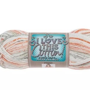 Peut inclure: Une pelote de fil panaché présentant une palette de couleurs blanc, pêche doux et gris clair. Une étiquette centrale en papier affiche le texte I LOVE THIS COTTON! SUPER SOFT... SUPER SAVINGS! PRINT, orné de petits cœurs sur fond bleu sarcelle.