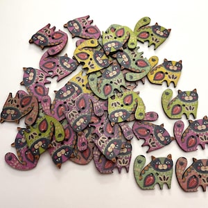 May include: A collection of flat wooden buttons shaped like sitting cats. Each button features a two-hole design and is decorated with intricate, colorful patterns in shades of green, purple, yellow, and pink, showcasing stylized feline features.