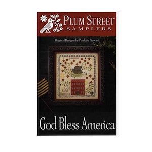 May include: A framed cross-stitch sampler with the text "God Bless America." The sampler features a patriotic design with a house, hat, and floral elements. The Plum Street Samplers logo is at the top.