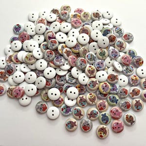 May include: A collection of wooden buttons, some plain white and others decorated with colorful fish designs. The fish buttons feature various colors and patterns, including red, blue, yellow, and pink. Each button has two holes for sewing.