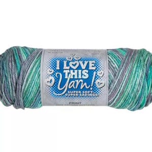 May include: A skein of variegated yarn featuring a blend of teal, mint green, and grey fibers. The center paper label displays the text I LOVE THIS YARN! SUPER SOFT SUPER SAVINGS! PRINT FREE PATTERN INCLUDED with small heart icons surrounding the text.