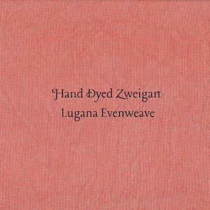 May include: A square of coral-colored fabric with the text "Hand Dyed Zweigart Lugana Evenweave" in black. The fabric has a textured appearance, suggesting a woven material, and the text is centered.