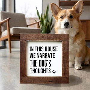 Puede incluir: Un letrero enmarcado en madera con el texto "IN THIS HOUSE WE NARRATE THE DOG'S THOUGHTS" en negro. Un perro Corgi marrón y blanco está sentado junto al letrero. El letrero tiene una huella de pata en la parte inferior derecha.