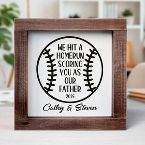 May include: A wooden sign with a baseball graphic and the text "We hit a homerun scoring you as our father 2025 Cathy & Steven".