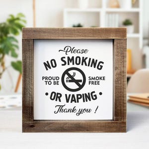 May include: A wooden framed sign with the words "Please NO SMOKING OR VAPING Thank you!" in black text. The sign also includes a graphic of a cigarette with a line through it. The frame is made of dark brown wood.