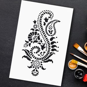 May include: A black and white stencil featuring a paisley design with intricate details. The stencil is on a white sheet of paper.