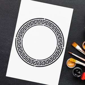Könnte beinhalten: Ein weißes Blatt Papier mit einem schwarzen griechischen Schlüsselranddesign. Das Papier liegt auf einer schwarzen Oberfläche mit Pinseln und Farbtöpfen.