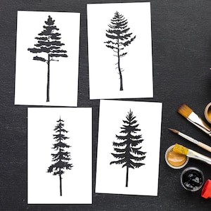 May include: Four black and white tree silhouette prints on white paper. The tree designs vary in shape and style, with detailed branches and trunks. The prints are arranged on a black surface, with paintbrushes and paint pots visible in the corner.