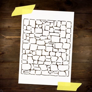 May include: A white stencil with a black design of a brick pattern. The stencil is taped to a brown wooden surface.