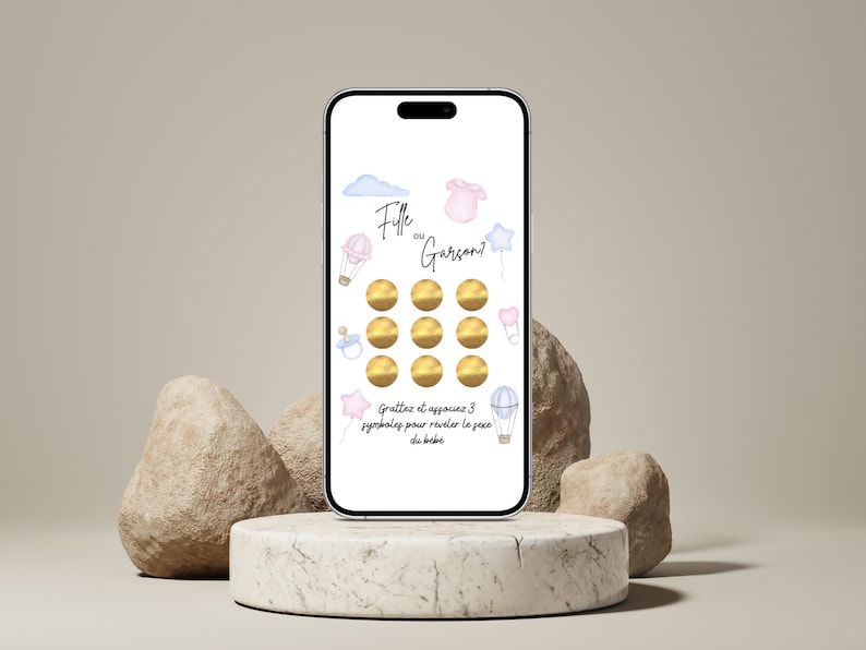 May include: A smartphone displays a gender reveal game with the text "Fille ou Gar&ccedil;on?" (Girl or Boy?). The screen features watercolor illustrations of a cloud, a onesie, a star, a pacifier, and hot air balloons. The game has golden scratch-off circles.