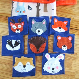 Può includere: Un set di quadrati di animali in feltro con una custodia abbinata. Ogni quadrato blu presenta una diversa creatura del bosco, tra cui un cervo, un lupo, una volpe, un tasso, un riccio, un orso, uno scoiattolo e un coniglio. La custodia arancione ha il nome "JOYA ANABEL" stampato.