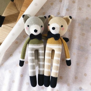 May include: Two crocheted stuffed animals in the shape of foxes. One fox is green and white striped and the other is yellow and white striped. Both foxes have black eyes, black noses, and black bow ties.
