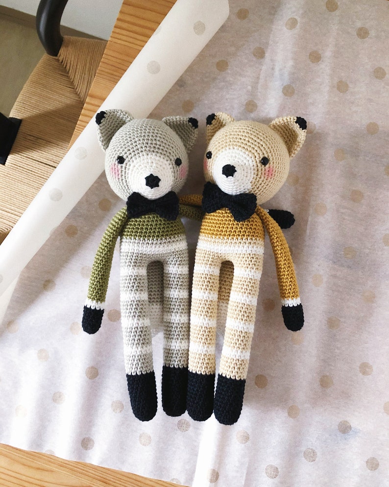 May include: Two crocheted stuffed animals in the shape of foxes. One fox is green and white striped and the other is yellow and white striped. Both foxes have black eyes, black noses, and black bow ties.