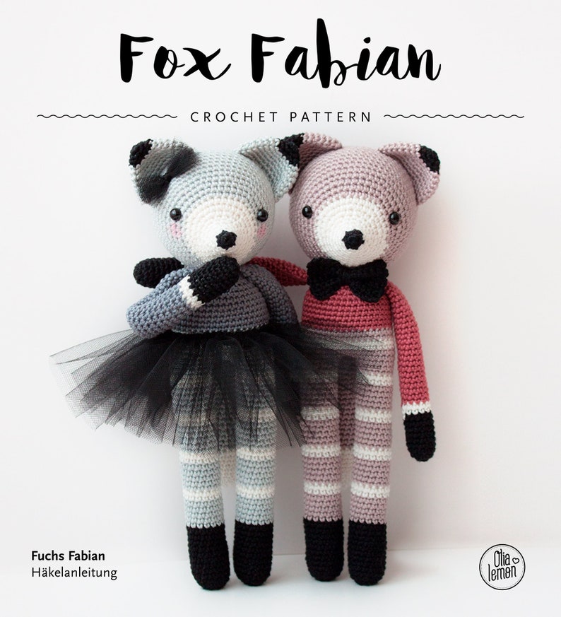 May include: Two crocheted fox amigurumi toys, one gray and white with a black tutu and the other pink and white. The toys are standing side by side on a white background. The text "Fox Fabian Crochet Pattern" is at the top of the image.