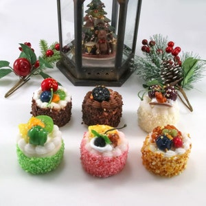 Op de afbeelding: Zes mini-taarten versierd met verschillende vruchten, chocolade en sprinkles. De taarten zijn gerangschikt op een wit oppervlak.